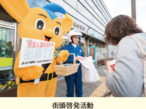 街頭啓発活動。警察官とピーポくんが通行人にリーフレット等を配っている様子の写真